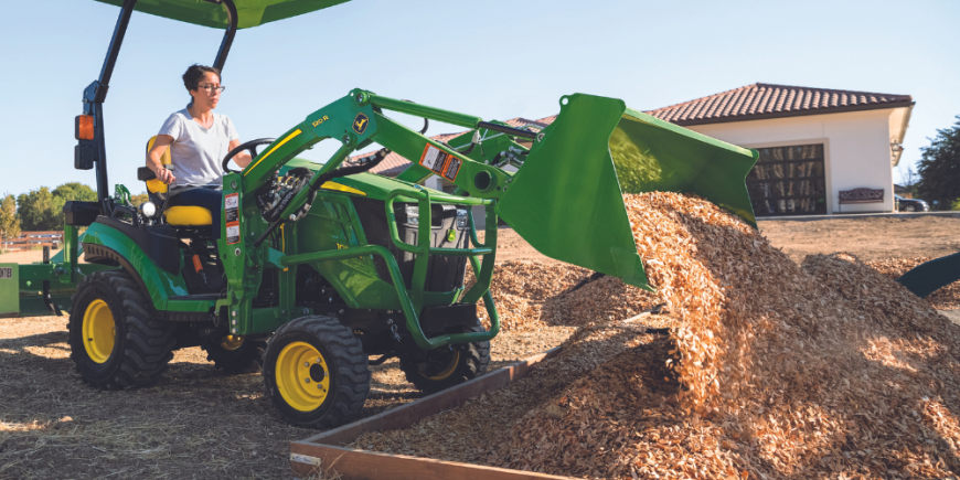 A woman dumps a load of wood chips using her John Deere tractor.